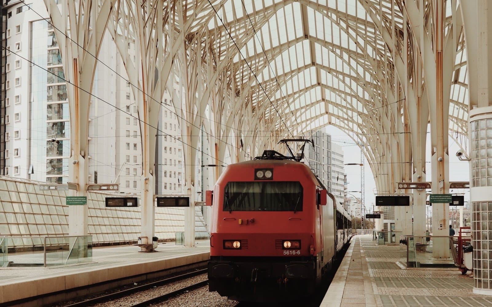 Red passenger train arriving at a modern Lisbon railway station