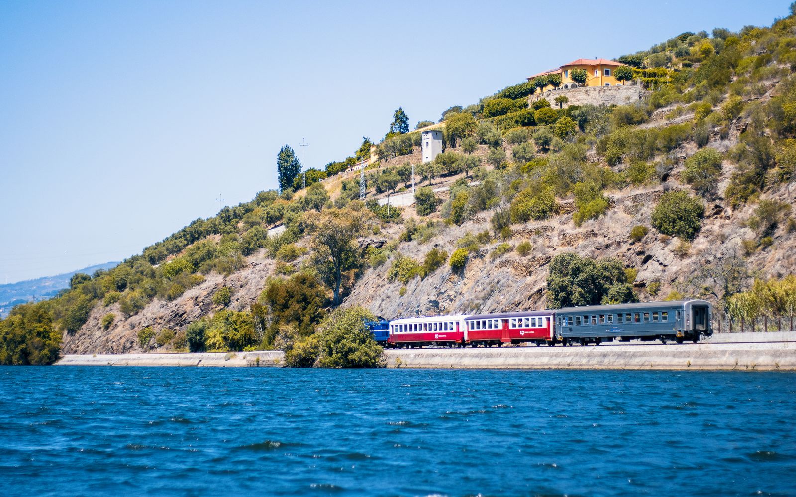 Passenger train travelling beside the Douro River below green hills