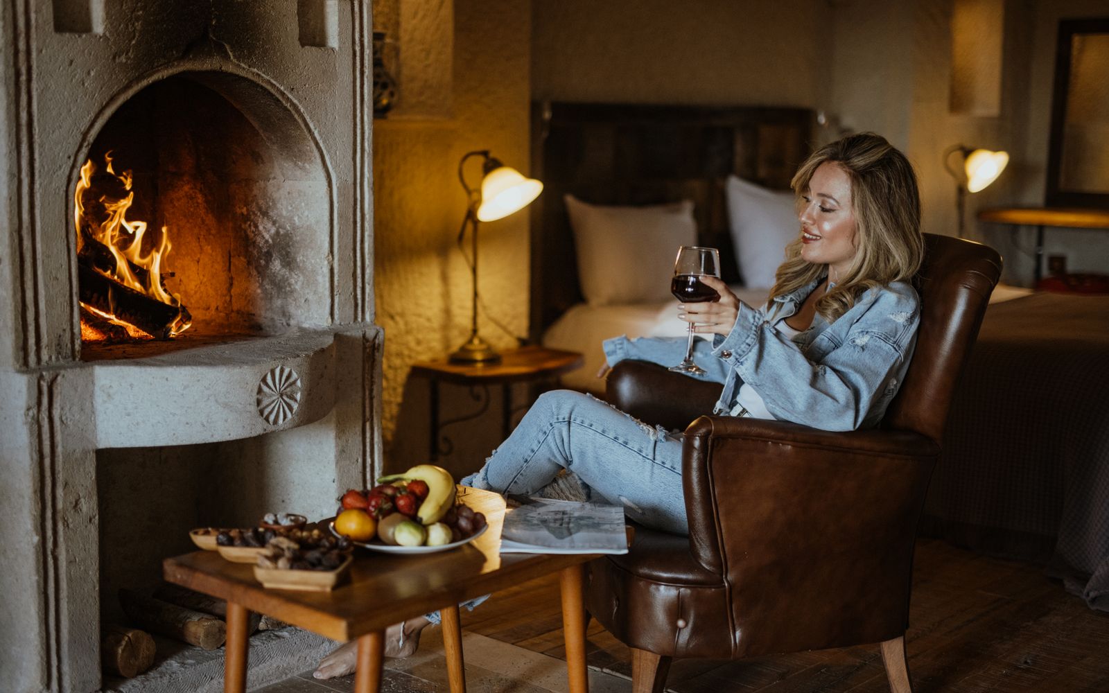 Woman relaxing with a glass of wine beside a fireplace in a hotel room